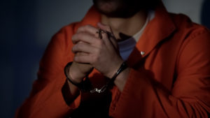 Imprisoned male in handcuffs holding cross and praying